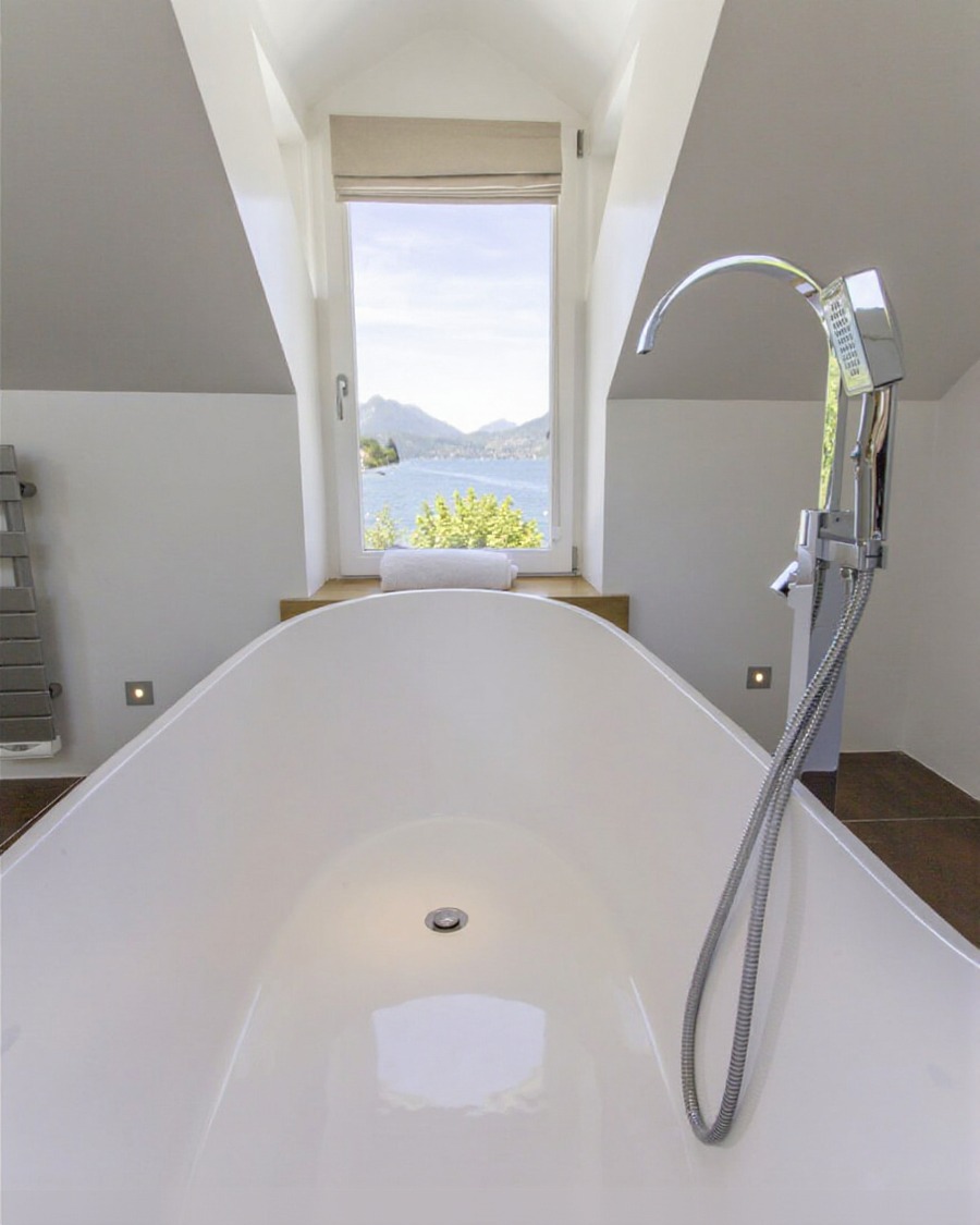 Freestanding bath beside a tall window with a lake-and-mountain view
