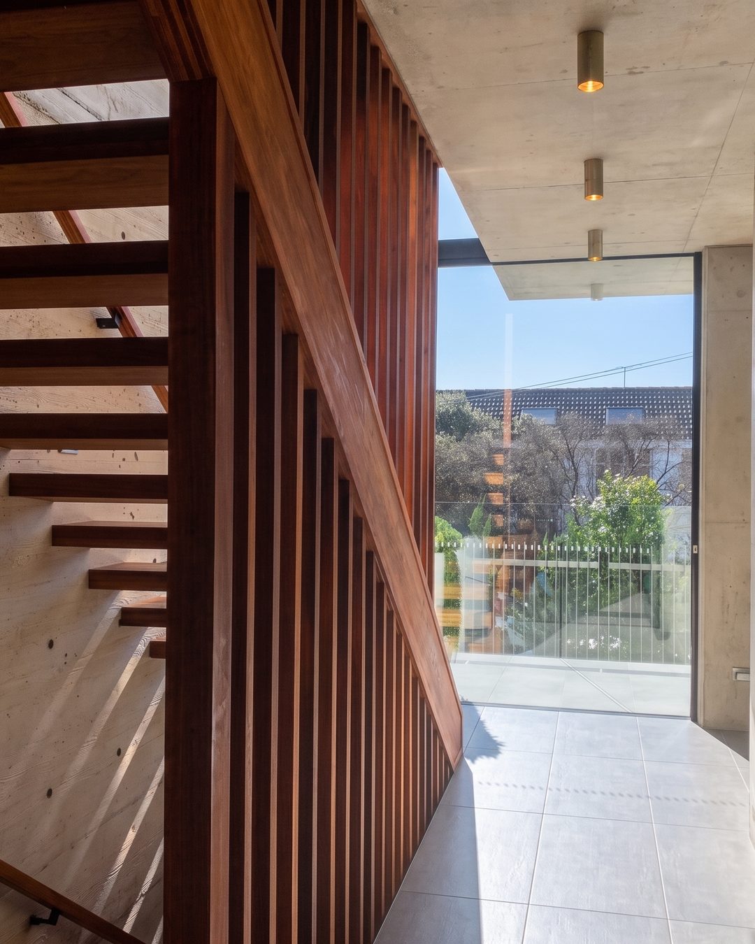 Board-formed concrete stairwell with floating timber treads, a slatted timber screen and full-height glazing to a landscaped garden