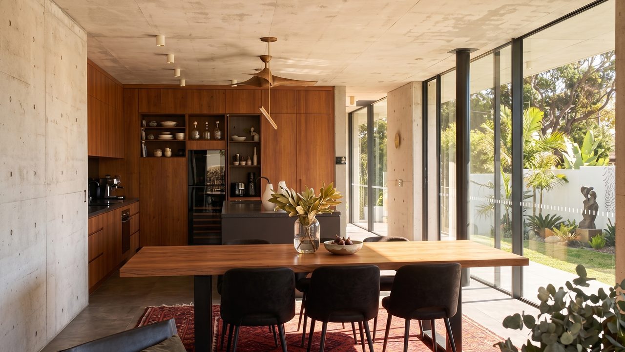 Concrete and timber dining space with floor-to-ceiling glazing to a landscaped garden