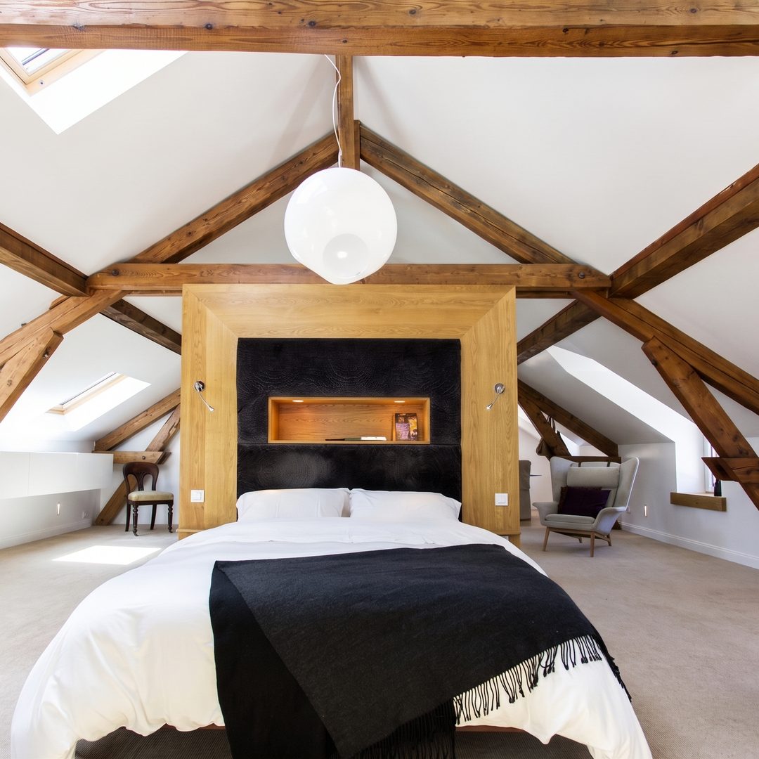 Attic conversion bedroom with exposed timber trusses and a feature bedhead